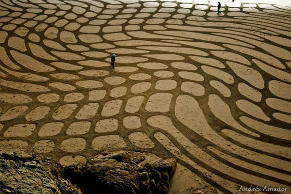 By raking up the wet sand at low tide, he is able to make contrasting sand colors.