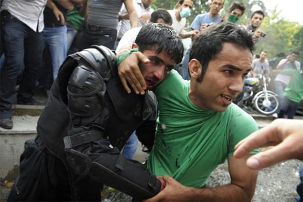 15.) Civilians protect an Iranian police officer after he is beaten by rioters.
