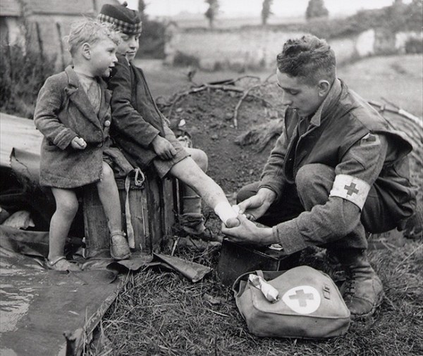 3.) A medic bandages a child's foot while his brother watches.