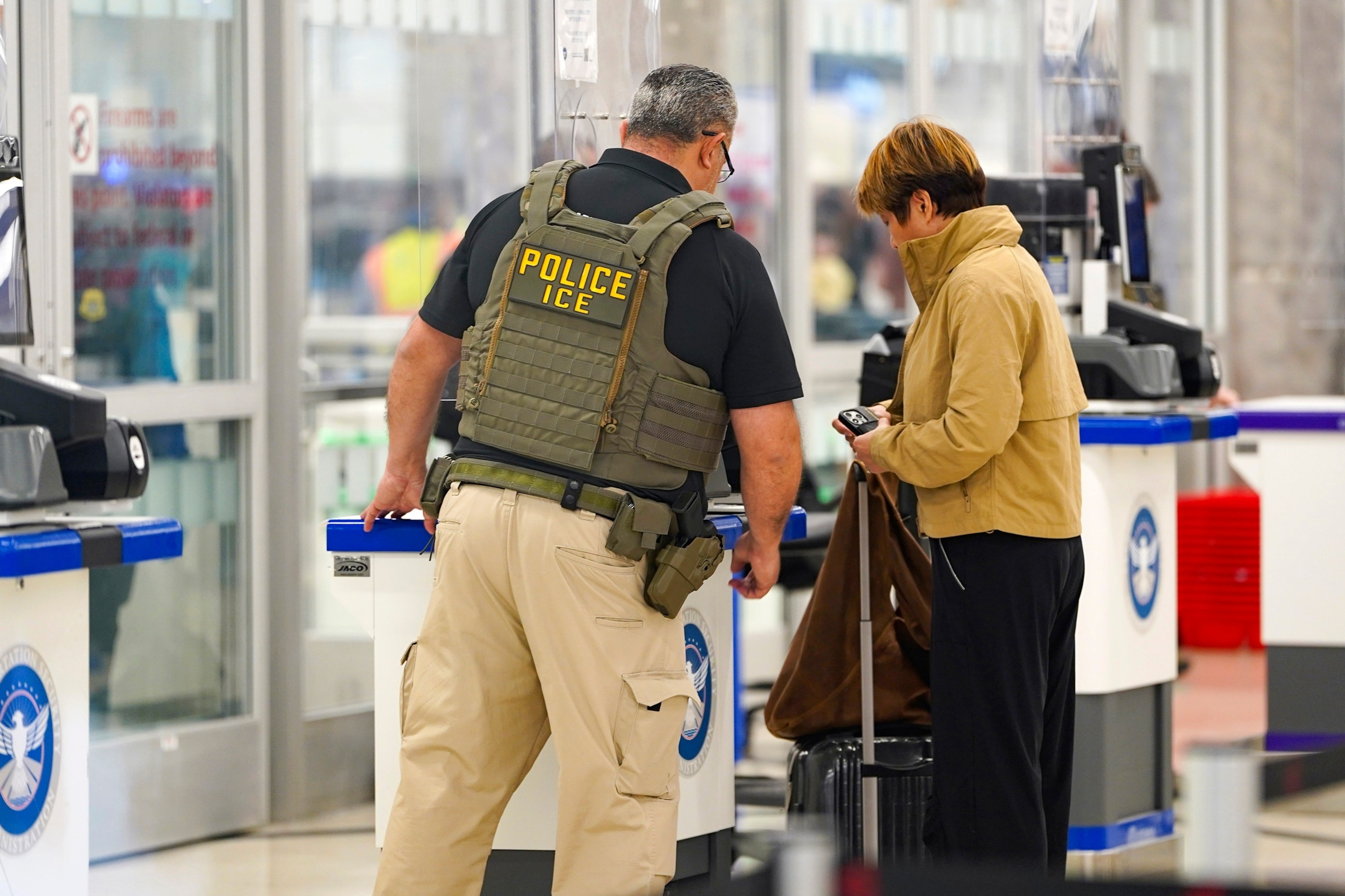 ICE agents at an airport checkpoint interviewing a traveler.