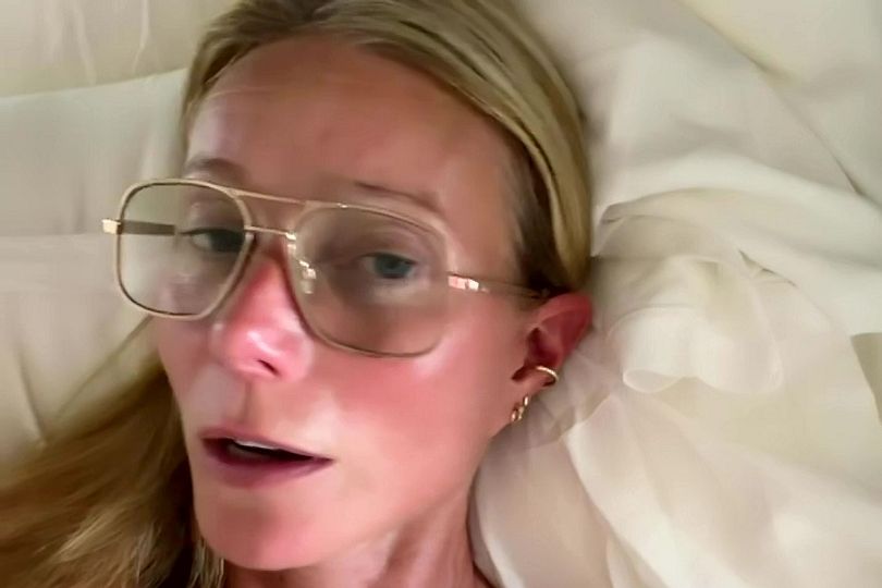 Paltrow appearing topless in bed with gold-rimmed aviator sunglasses.