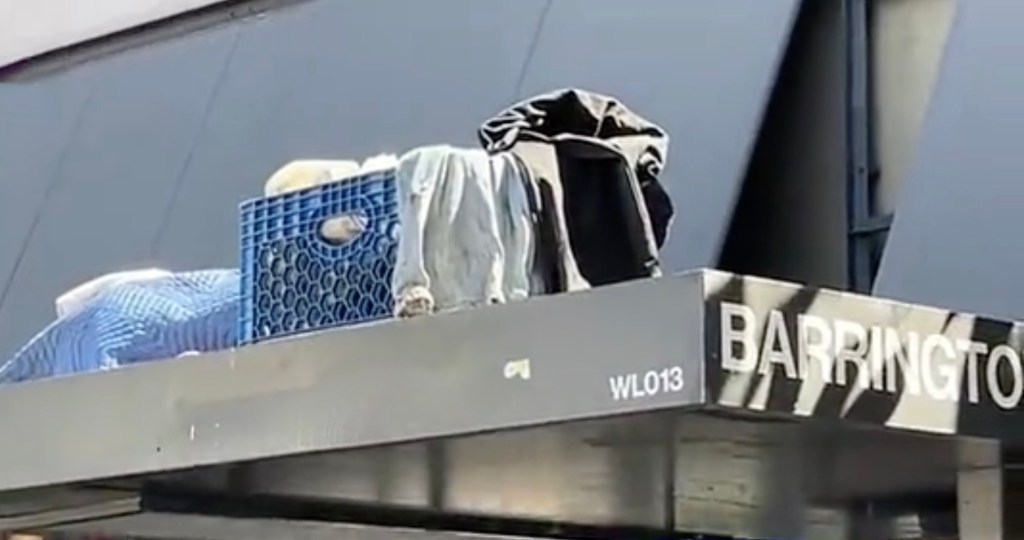 Homeless man makes a camp, complete with shopping cart, atop a bus shelter in upscale LA neighborhood