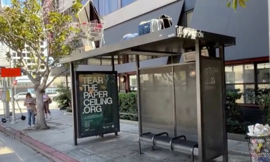 Homeless man makes a camp, complete with shopping cart, atop a bus shelter in upscale LA neighborhood